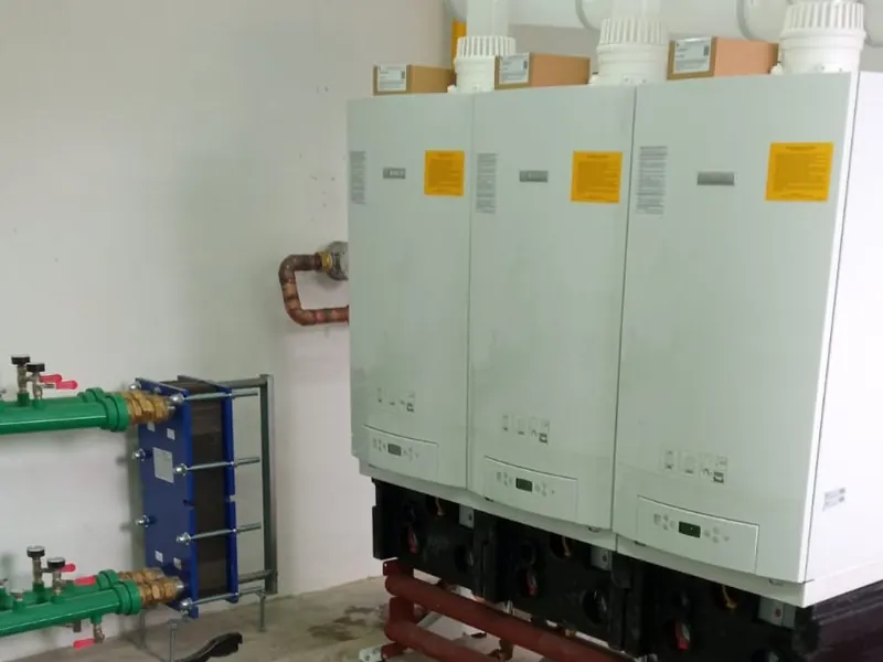 Batería de calderas murales en cascada con colector y bombas en una sala de calderas